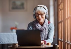 Shot of a senior woman using a laptop and headphones in a retirement home